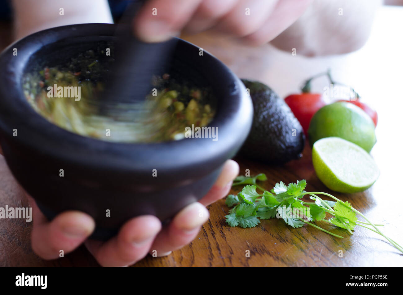 Making guacamole in a mortar with the ingredients showing on the background Stock Photo