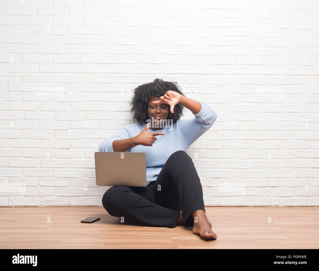Young african american woman sitting on the floor using laptop at home ...