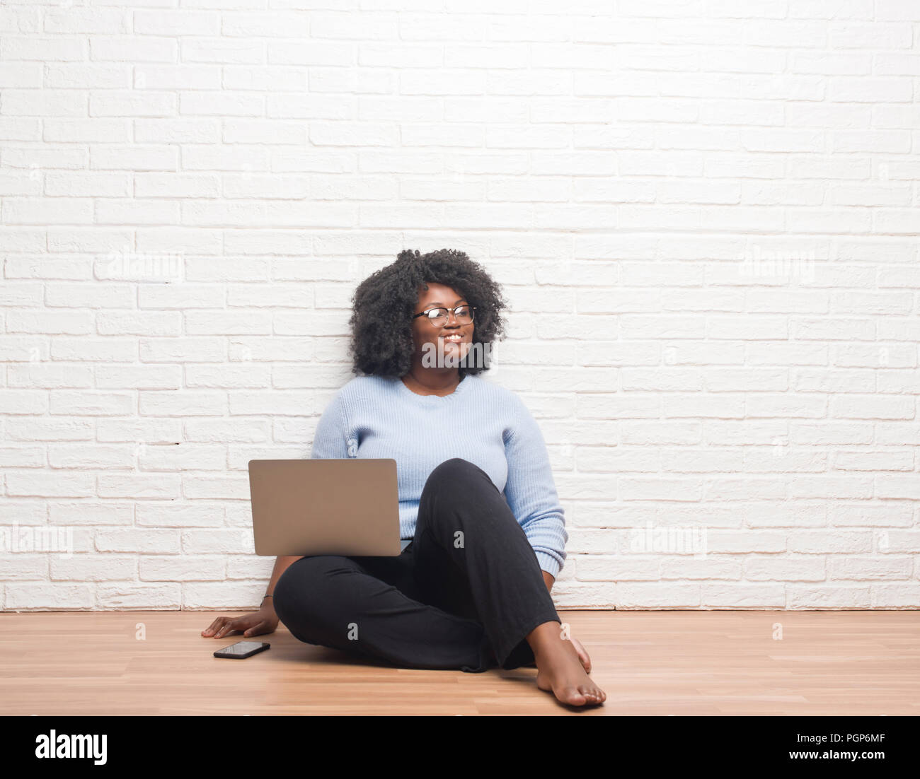 Young african american woman sitting on the floor using laptop at home ...