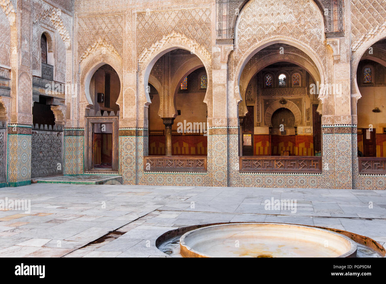 Moroccan mosque interior courtyard, with rows of arches featuring elaborate tiling and painted decoration. Location: Fes, Morocco Stock Photo