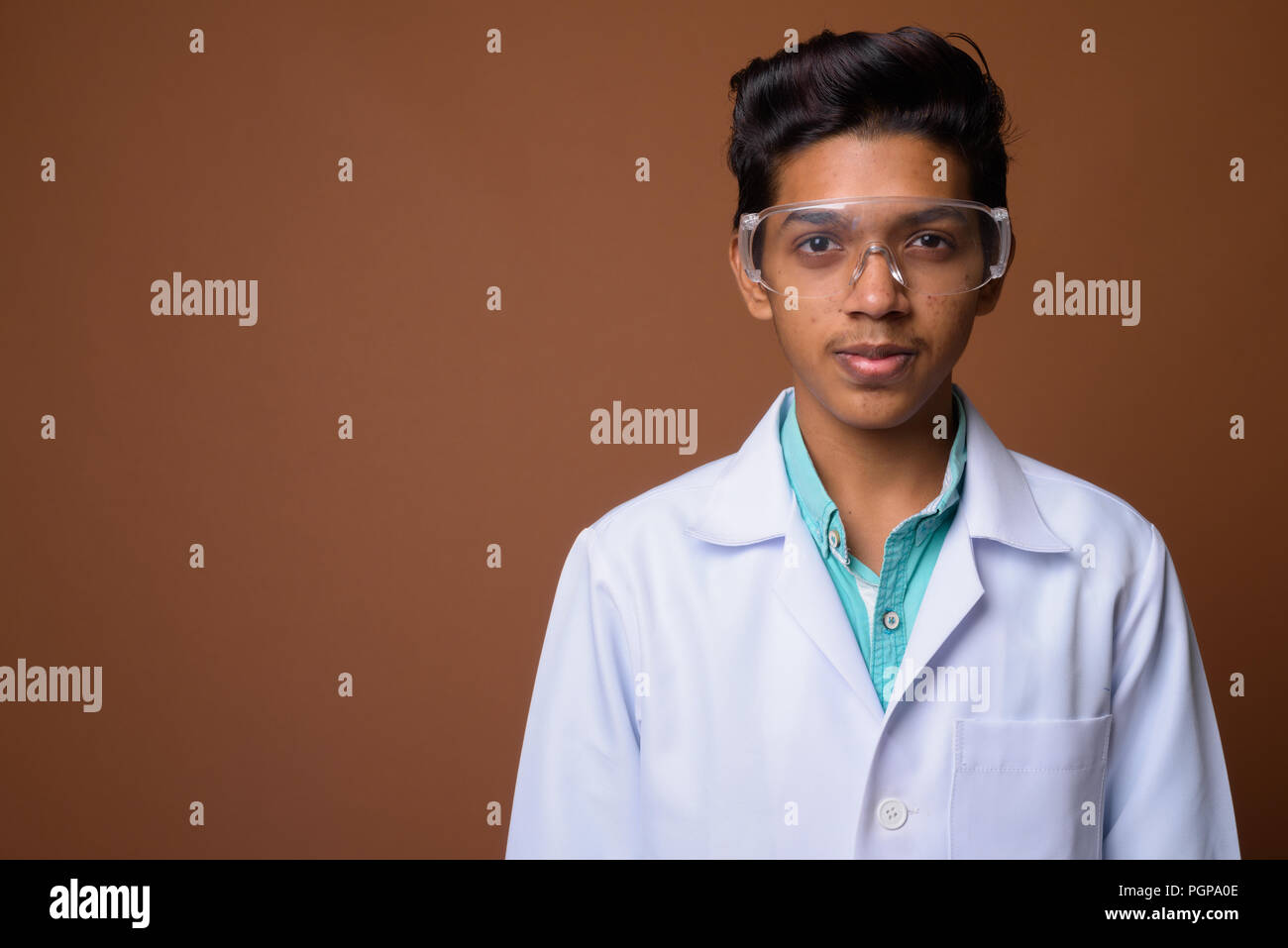 Young Indian boy doctor wearing protective glasses against brown Stock Photo