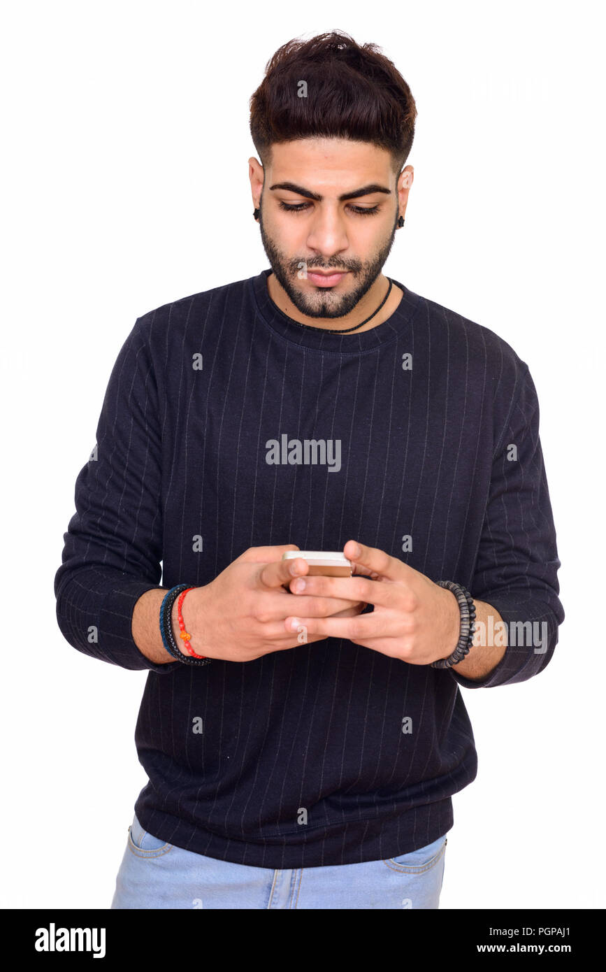 Studio shot of young handsome Indian man using mobile phone isol Stock Photo