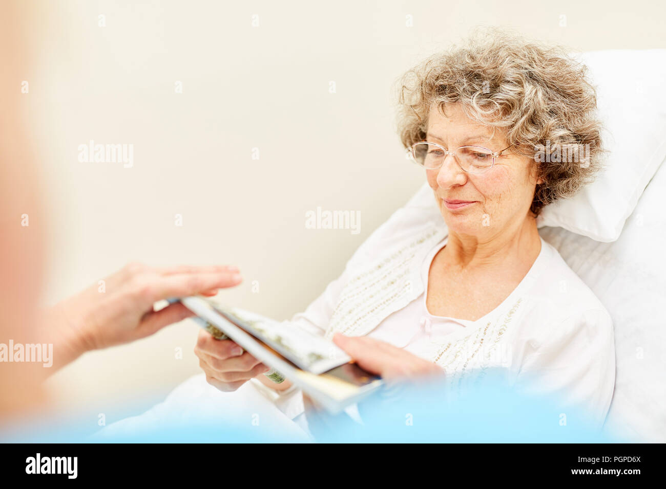 Senior woman in hospital bed while reading in nursing home or in