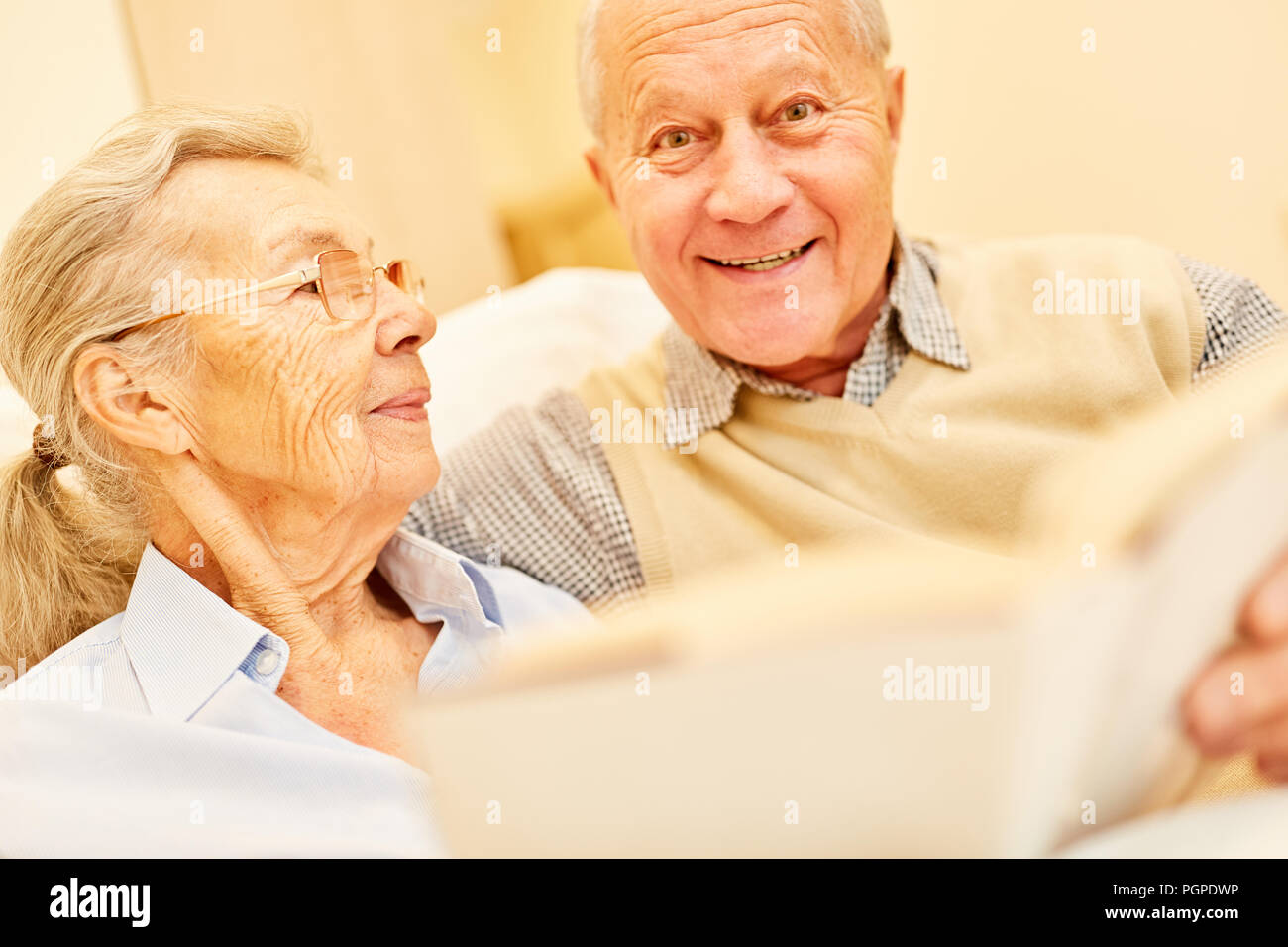 Happy senior man is reading to his wife from a book in the retirement home Stock Photo