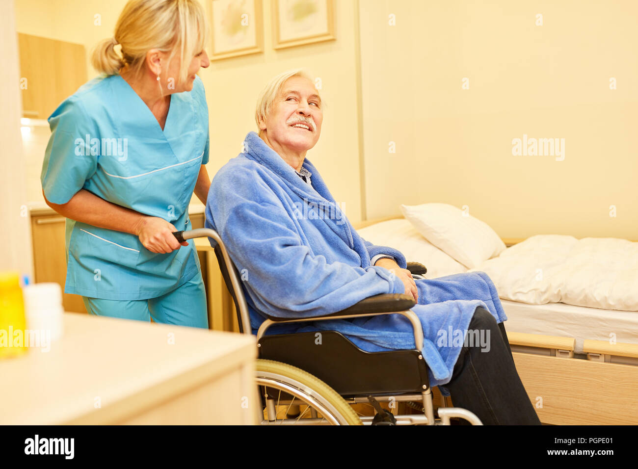 Caregiver pushes senior man in wheelchair in nursing home at retirement home Stock Photo
