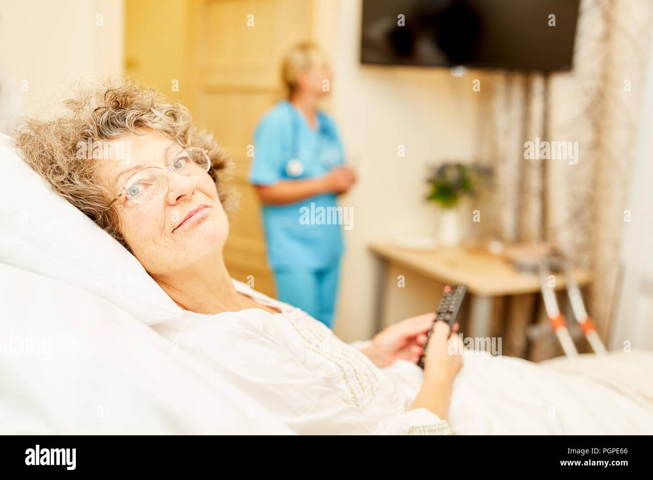 Bedridden senior woman with remote control in retirement home or