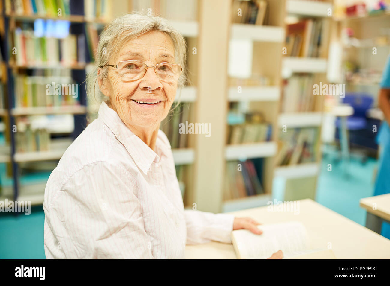 Old woman as a librarian with a book in a library in a retirement home Stock Photo
