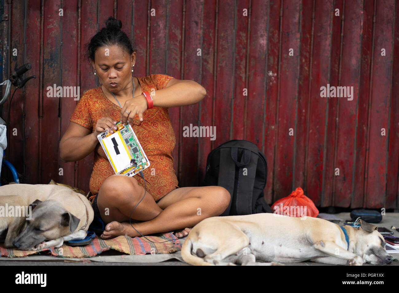 A woman repairs an electronic device along a sidestreet near to the Carbon Market,Cebu City,Philippines Stock Photo