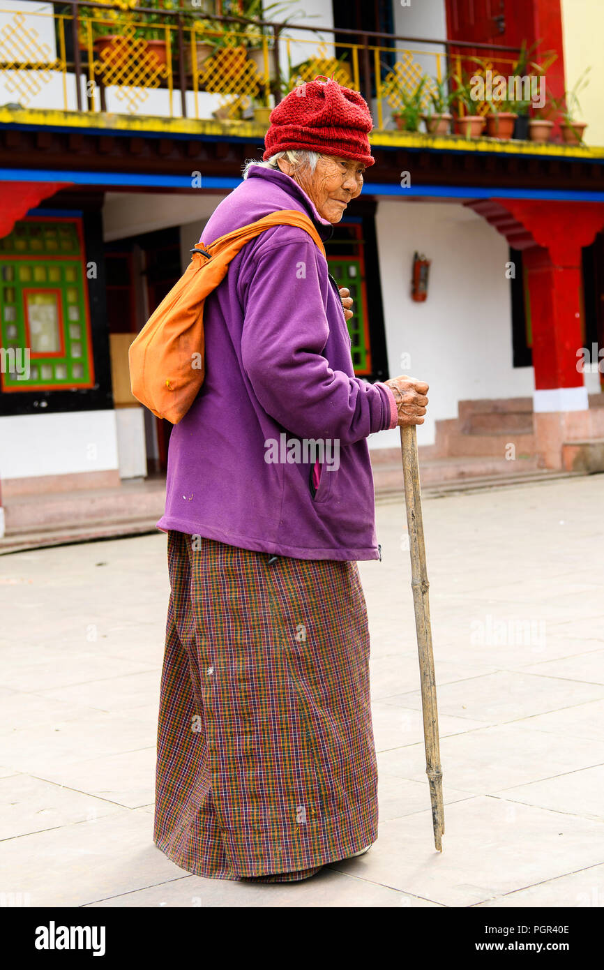 SIKKIM, INDIA - MAR 13, 2017: Unidentified Indian old woman in red hat and violet jacket carries an orange backpack and leans on a cane Stock Photo