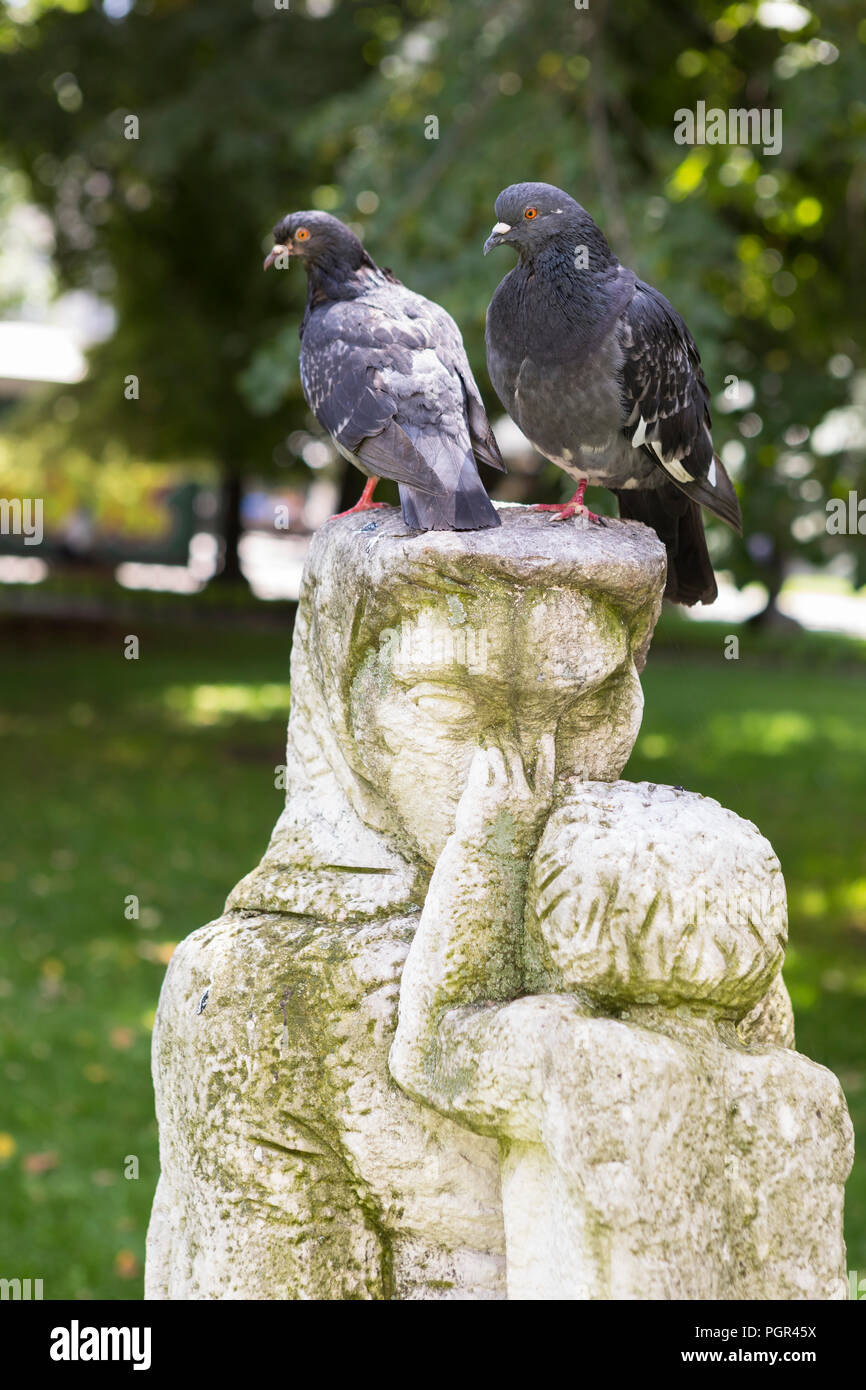 Two pigeons sitting on the head of a sculpture of a woman with child in the park Stock Photo