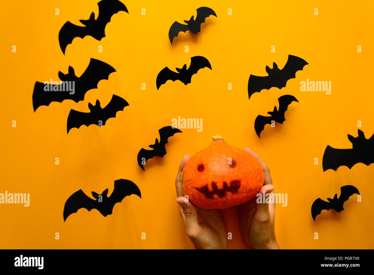 Woman's hand holding pumpkin with scary smile and black paper bats ...