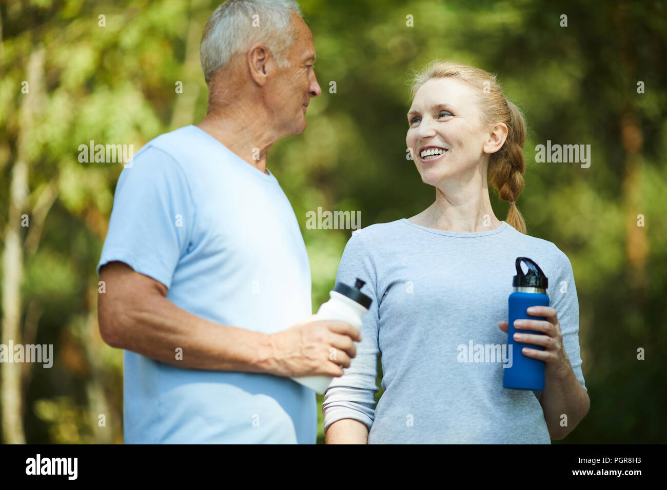 Healthy mature man and woman in activewear having refreshment after workout in natural environment Stock Photo