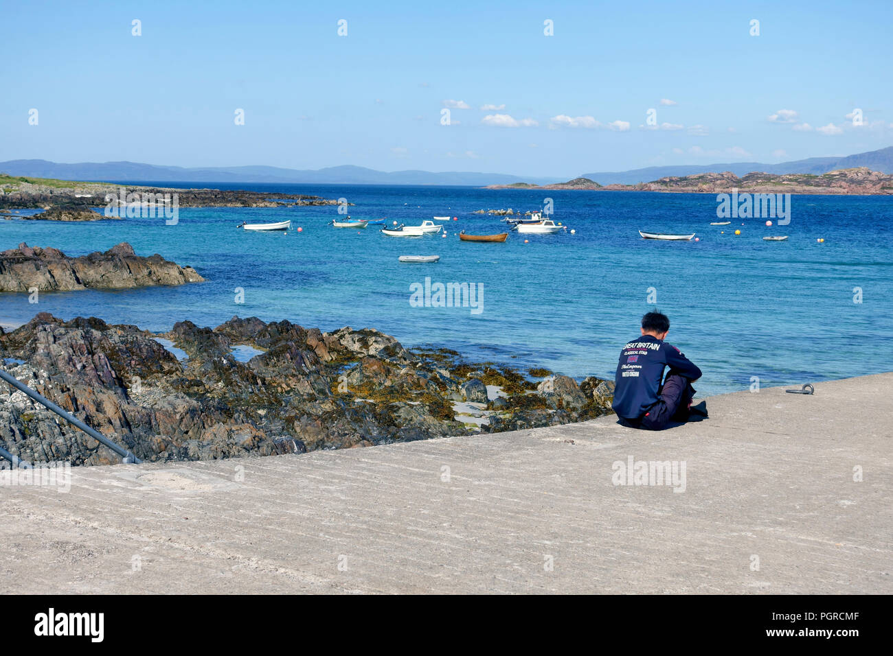 Man sitting peacefully on the slipway on Iona, taking in the peace and tranquillity of his surroundings in the Inner Hebrides of Scotland Stock Photo