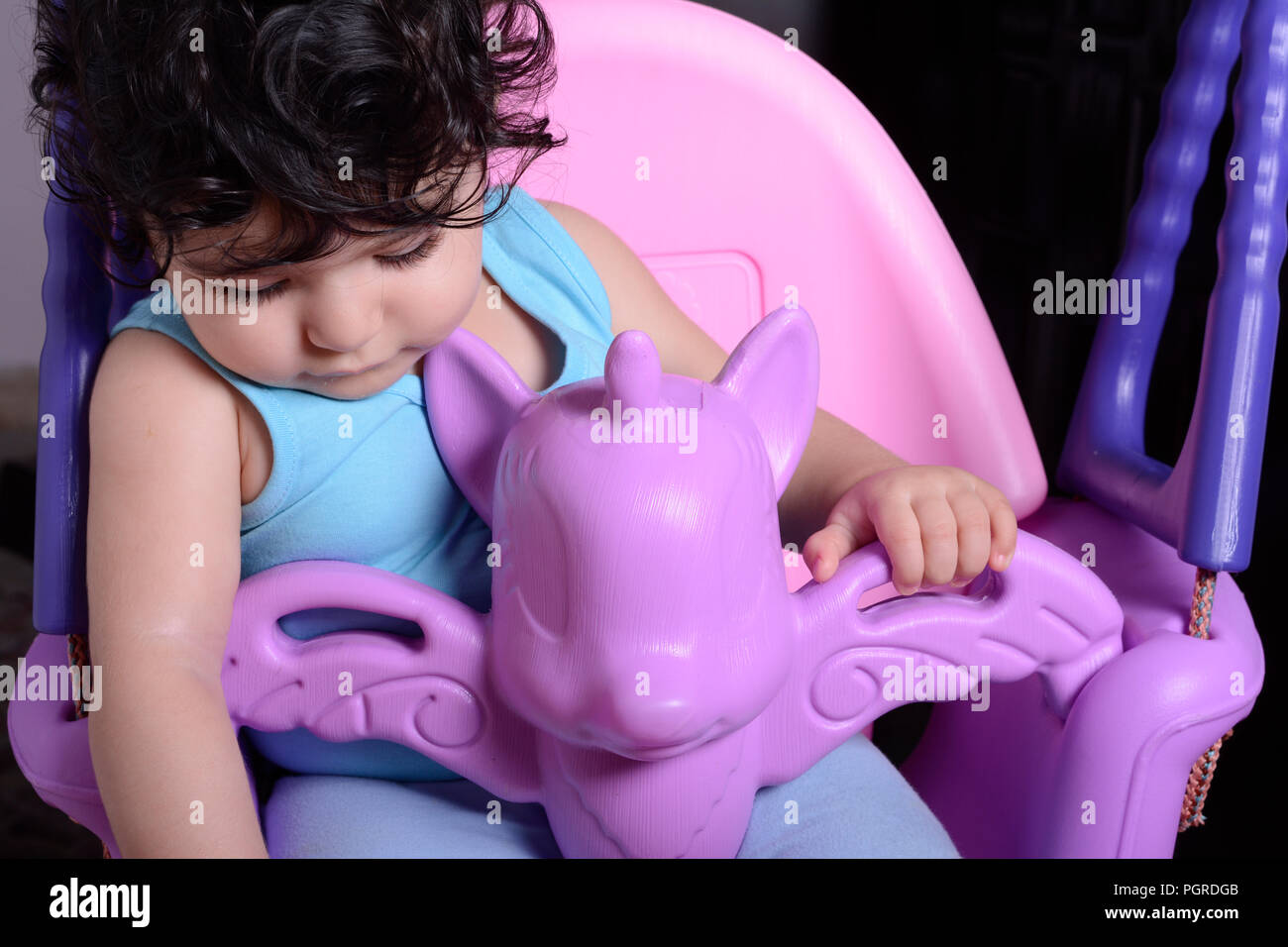 Portrait of a sleepy little baby girl on unicorn swing Stock Photo