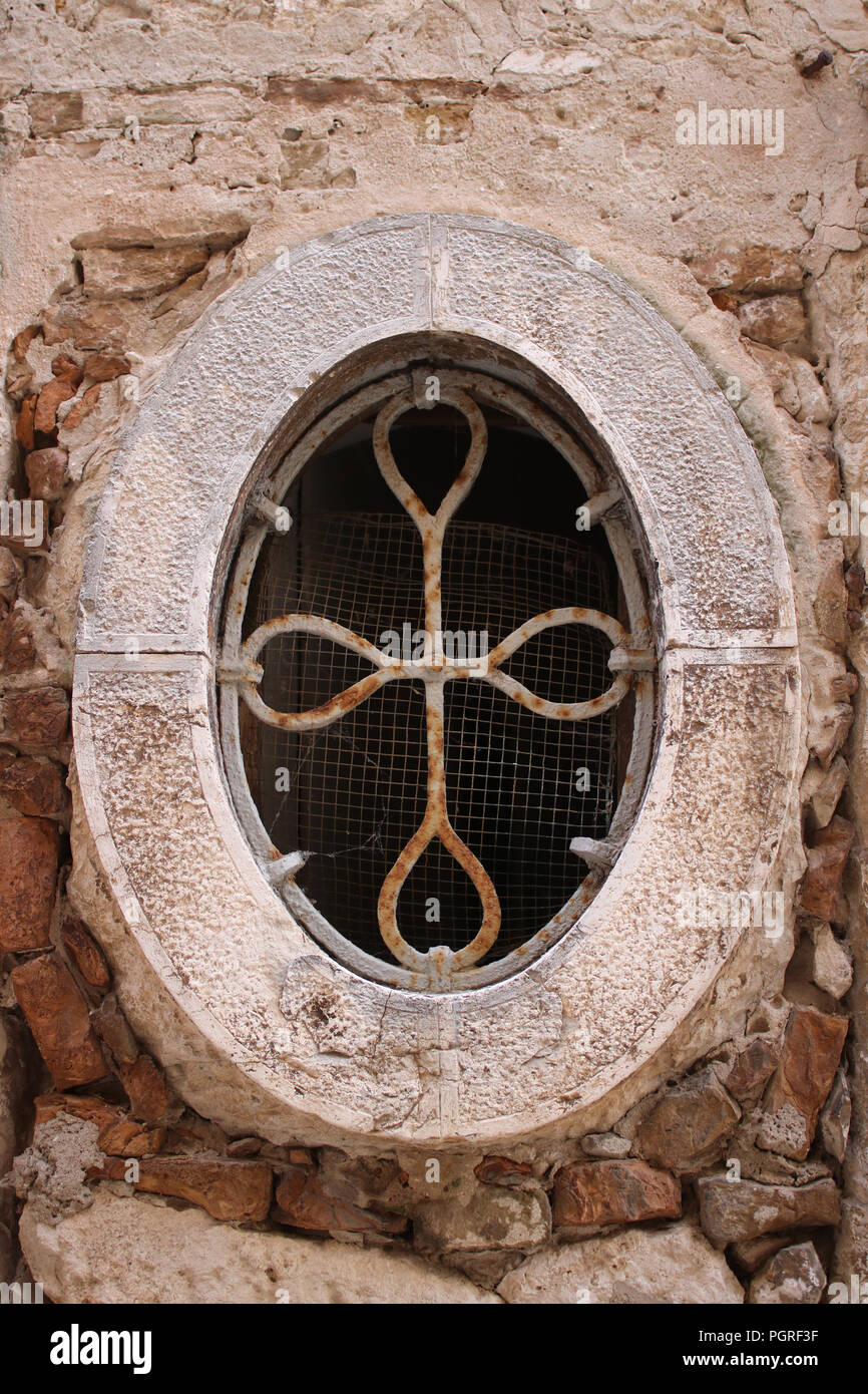 Interesting shaped old stone window frame with metal grille and wire mesh but no glass in on old building in Rovinj, Croatia. Stock Photo