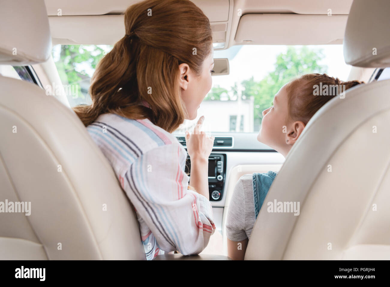 back view of mother showing something to daughter on passengers seat in