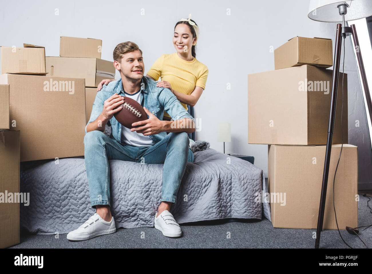 beautiful young couple sitting in bedroom of new home with american football ball Stock Photo