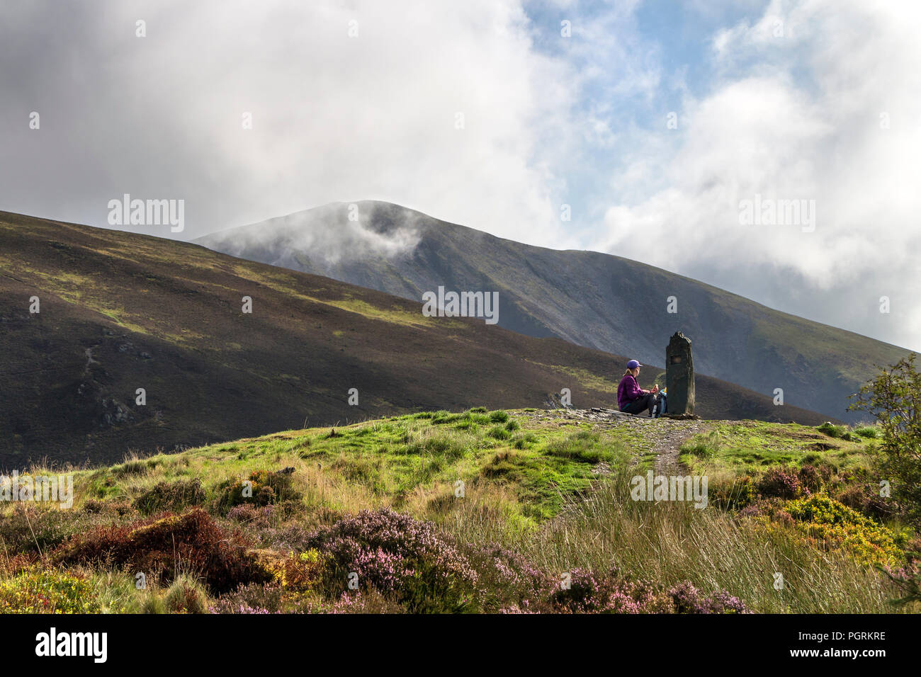 A Walker Enjoys a Break on the Summit of Dodd as Mist and Cloud Swirl Around the Summit of Little Man, Skiddaw Range, Lake District, Cumbria, UK. Stock Photo