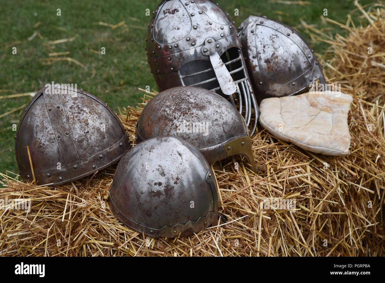 Helmets: a selection reproduction medieval helmets and a arming cap displayed on a straw bale Stock Photo