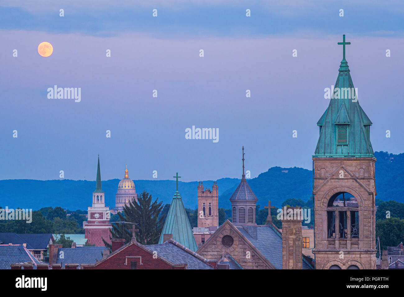The iconic church steeples line the skyline leading to the capitol building of Charleston, West Virginia as the full moon hangs in the evening sky. Stock Photo
