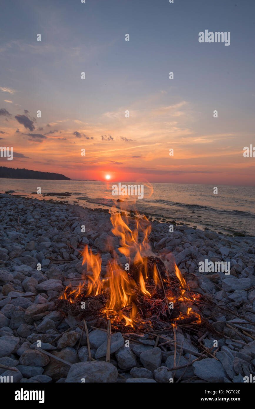 A fire burns near the sea at sunset. Stock Photo