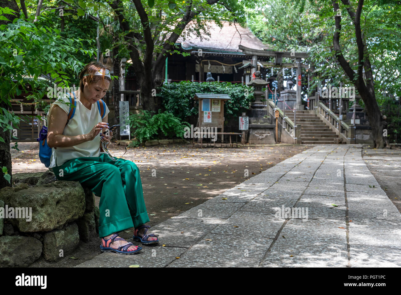 Taiwanese/Chinese/Asian woman checking her e-mail on her mobile phone while sitting in front of a shrine in a traditional Japanese garden in Tokyo Stock Photo