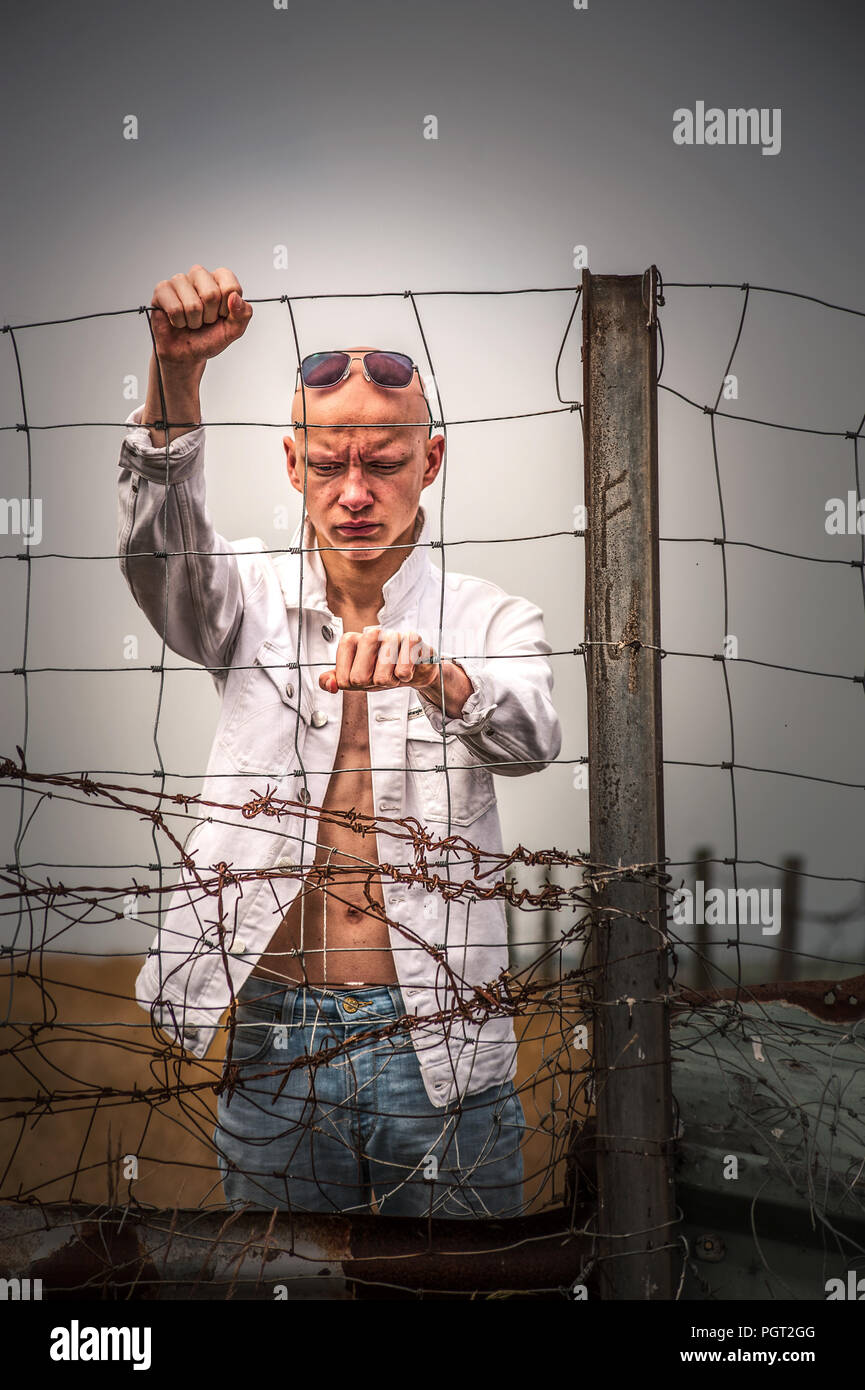 young angry man with bald head standing near wire fence Stock Photo