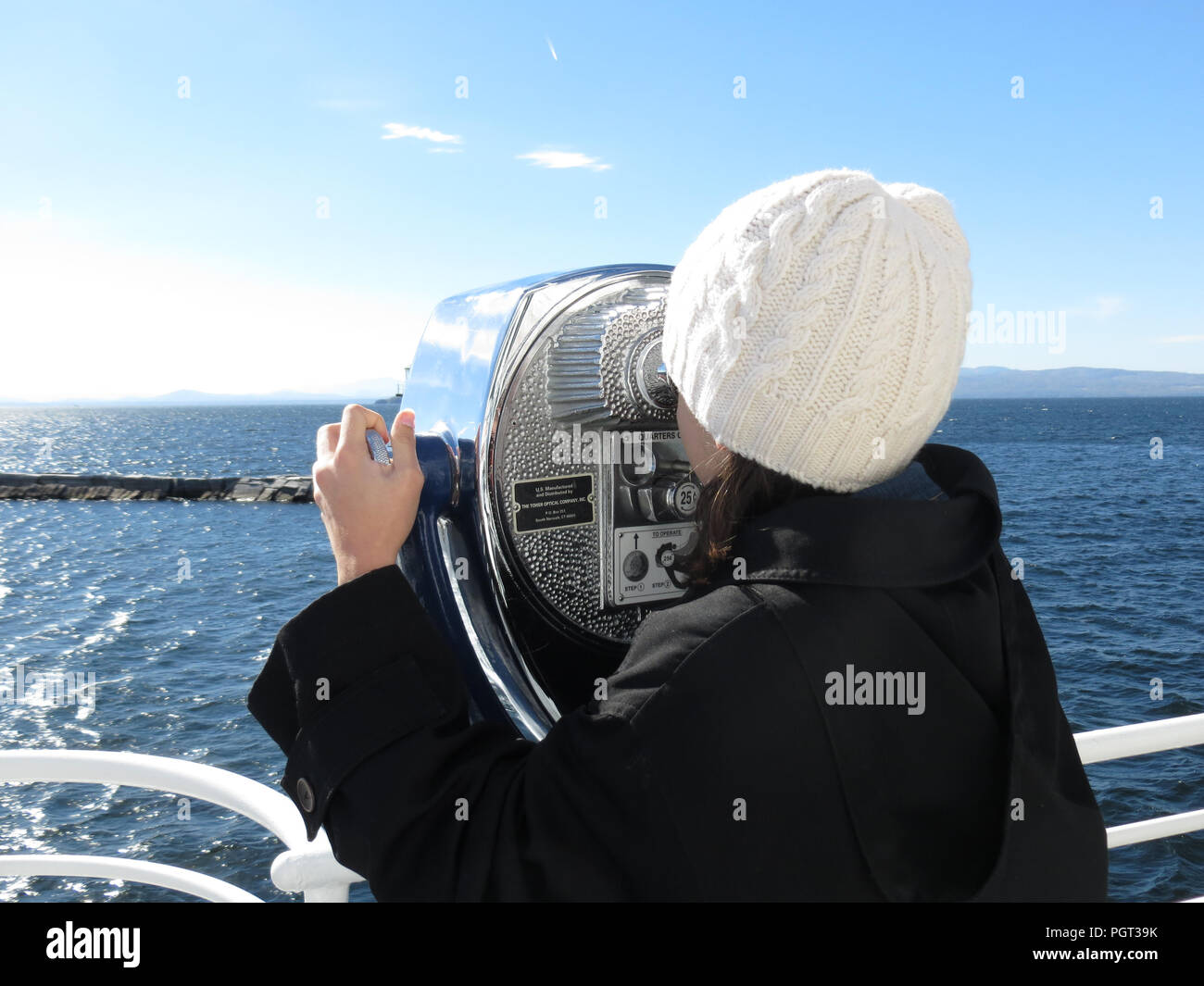Young girl, dressed for winter, looking through binoculars at the ocean from the deck of a boat. Stock Photo