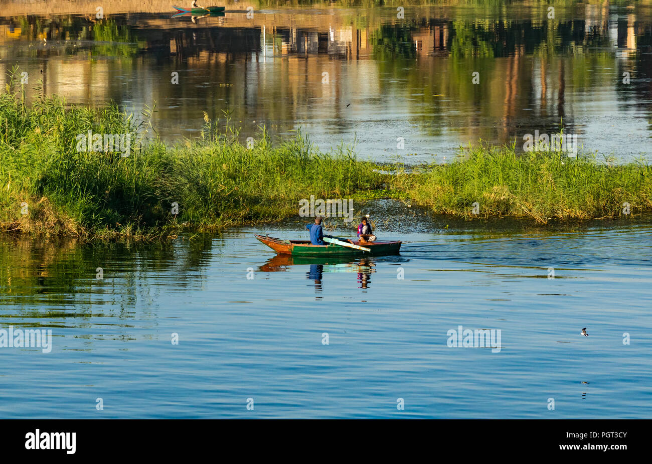 Egyptian local man rowing old boat with boy in early morning sunlight, with water reflections, Nile River, Egypt, Africa Stock Photo