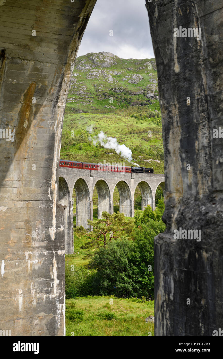 View of heritage Jacobite Steam Train through concrete columns of the Glenfinnan viaduct in the Scottish Highlands Scotland UK Stock Photo