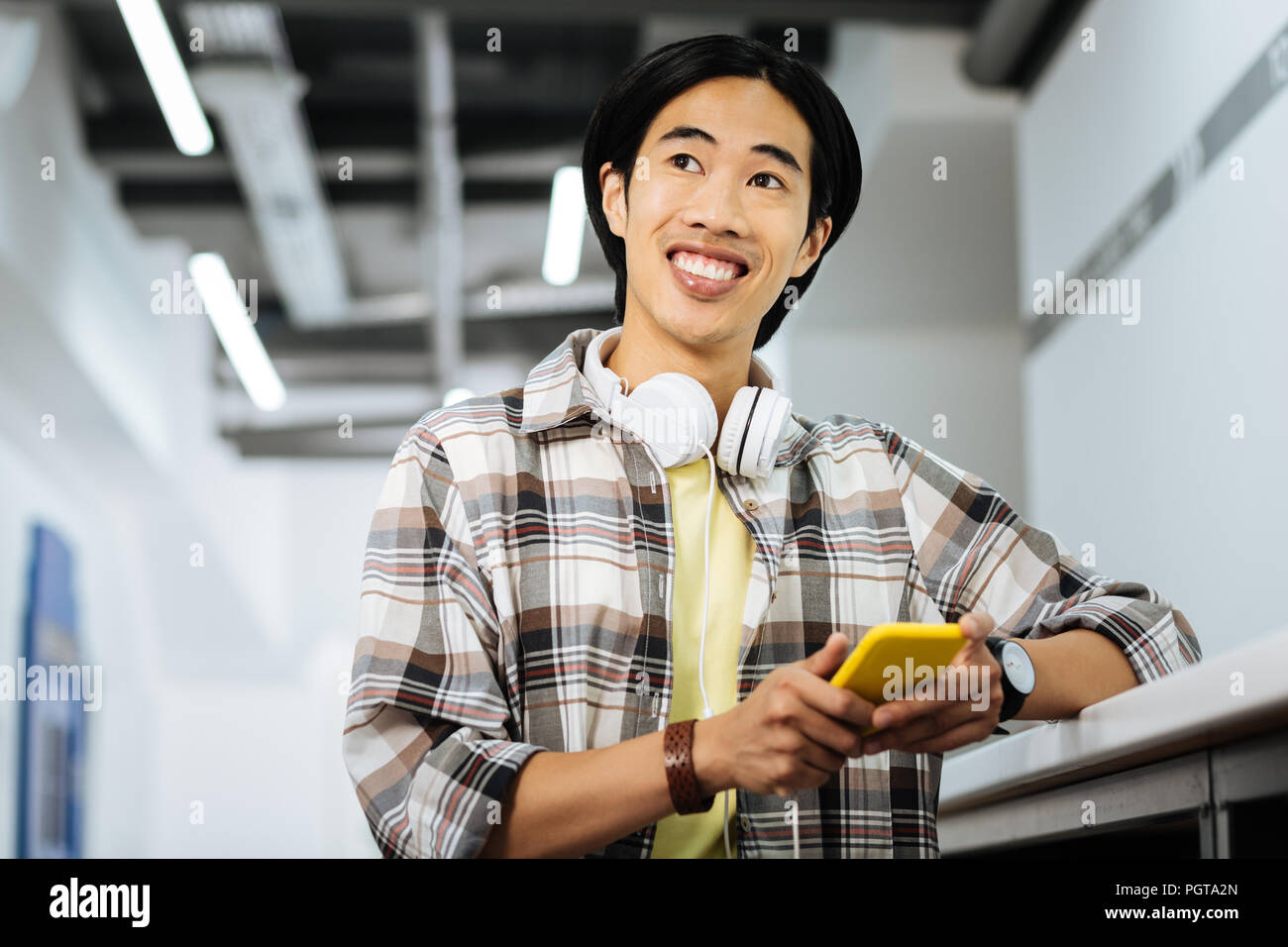 Happy Asian man smiling and holding his yellow gadget Stock Photo