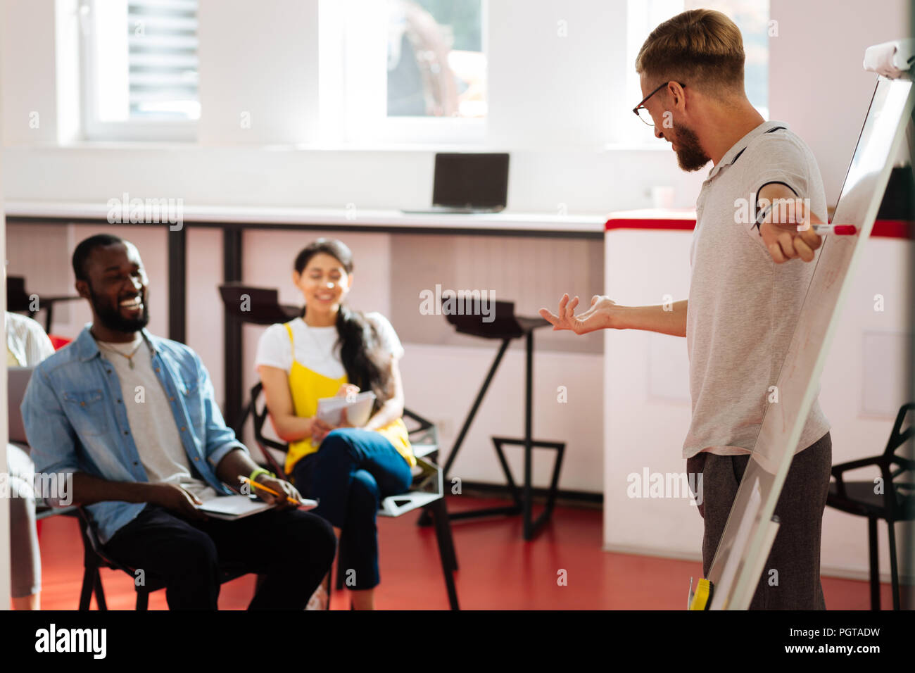 Positive teacher pointing to the flipchart and smiling to his students Stock Photo