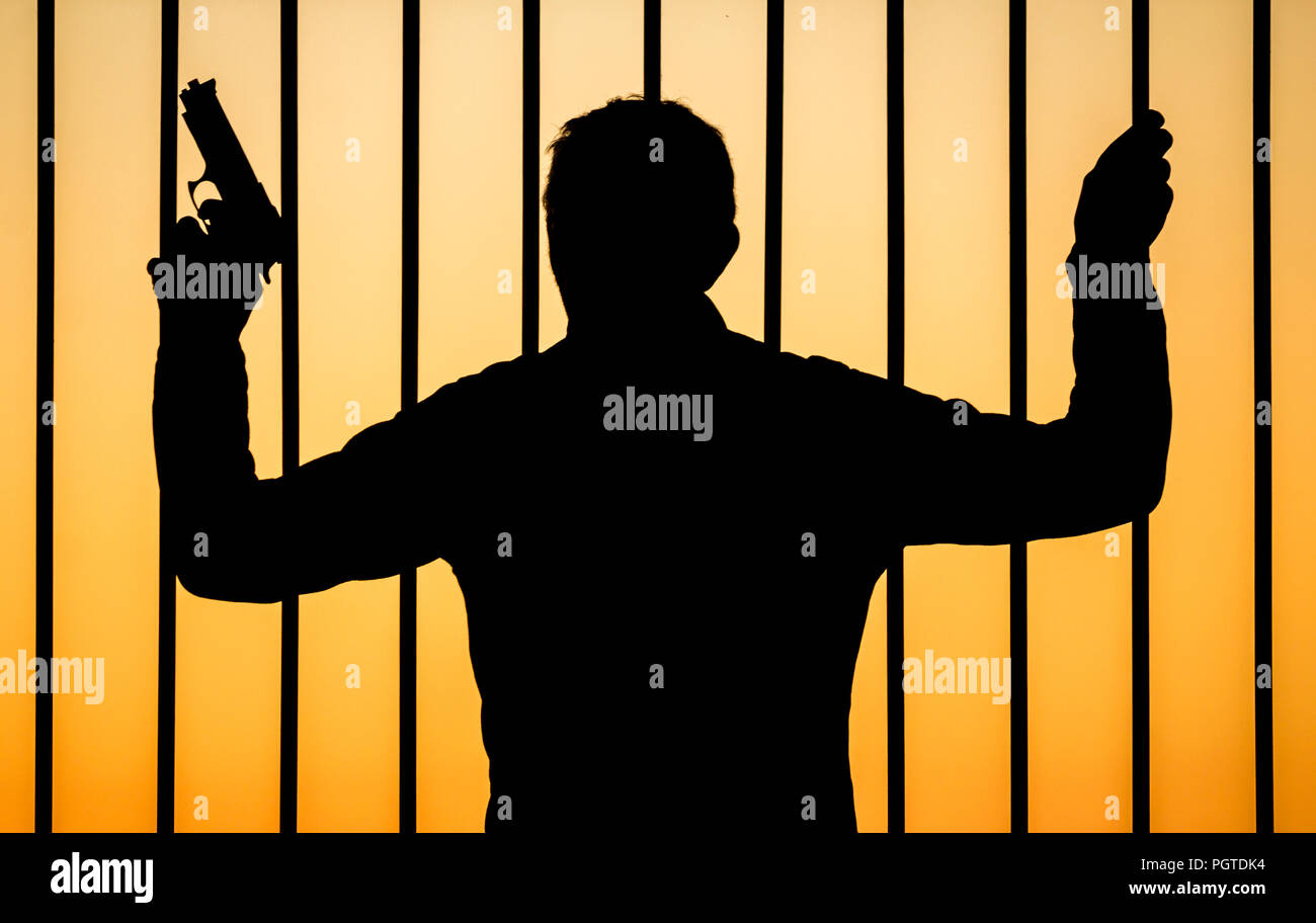 Silhouette of man holding gun looking through bars: concept image for gun crime, illegal arms/weapons, gang crime, guns in prison... Stock Photo