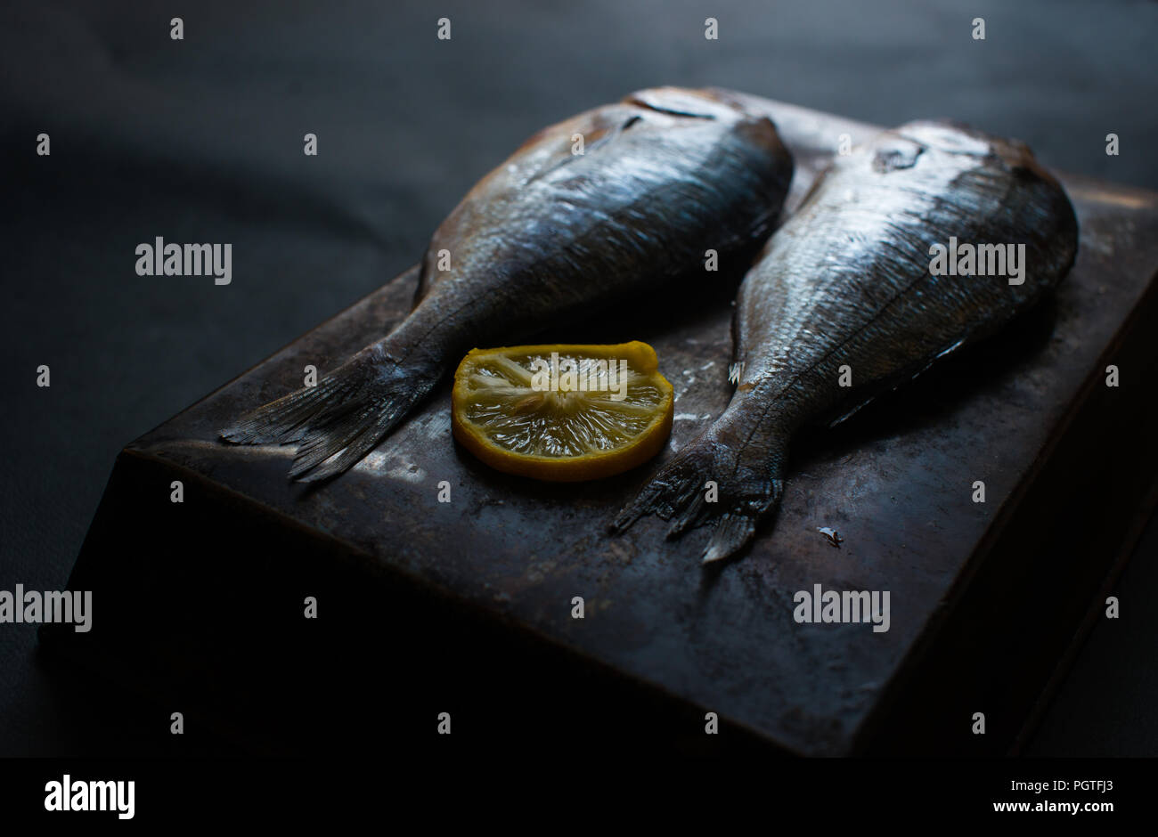 Two raw fish with lemon on the black background Stock Photo - Alamy