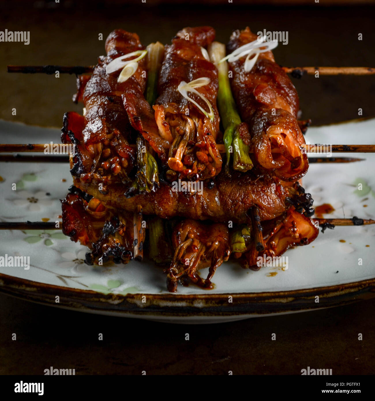 Bacon-wrapped Enoki Mushroom with a Maple-Sake Glaze on a light blue Japanese plate Stock Photo