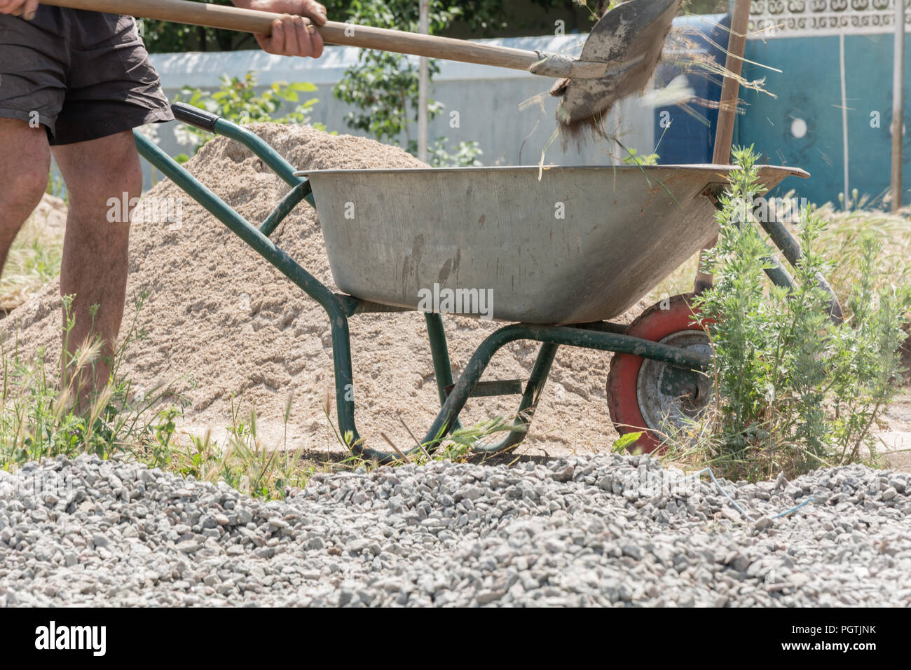 Worker use the shovel and fill the wheelbarrow with construction waste. Construction tools. Worker with shovel and the cart on wheels on building of t Stock Photo