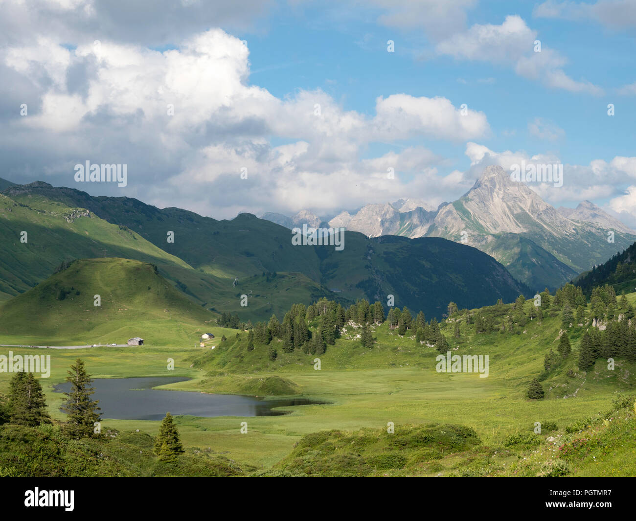 Sunlit Kalbelesee taken from the path to the Korbersee with cloud topped mountains on the Austrian, German border in the background, Austria Stock Photo