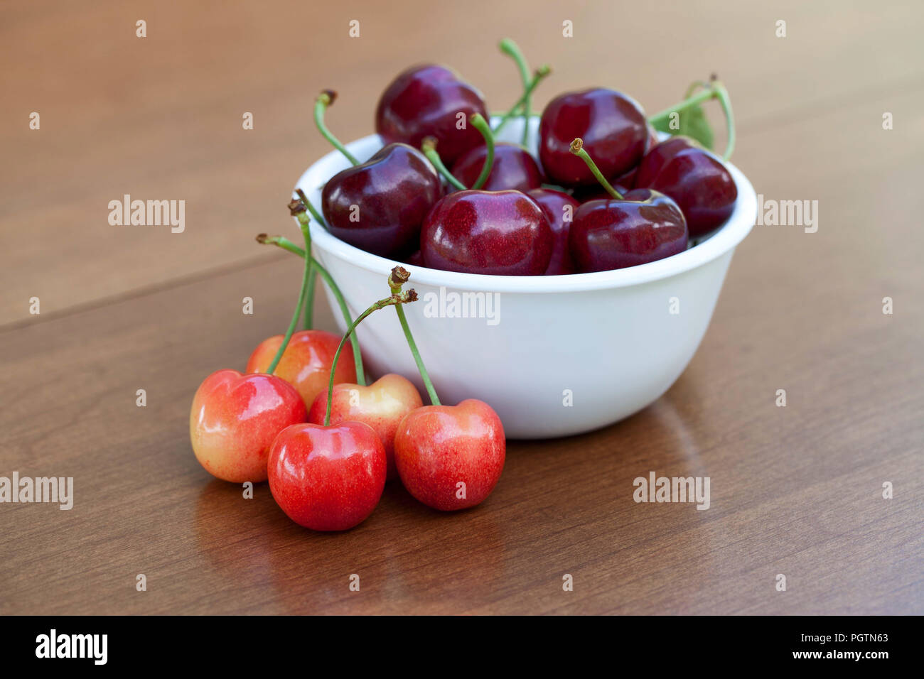 Red ripe cherries in a bowl and rainier cherries on table Stock Photo