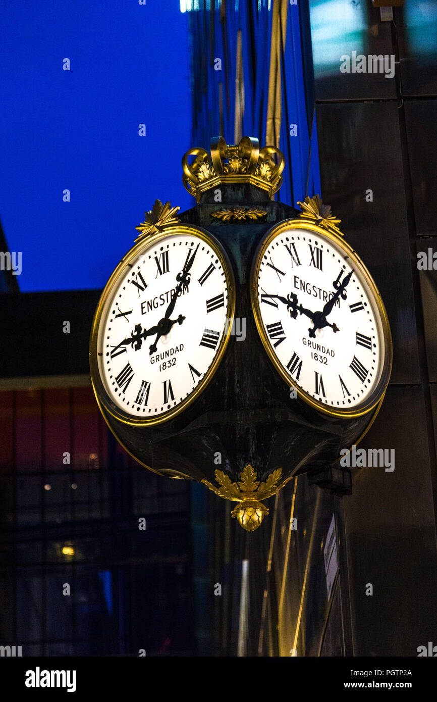 An illuminated gold ornate old-fashion Rob Engstrom clock with roman numerals at night time on Drottninggatan, Stockholm, Sweden Stock Photo