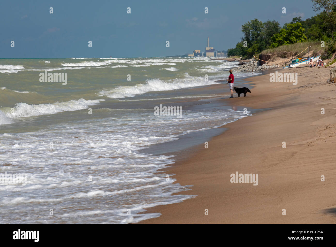 Beverly Shores, Indiana - A woman walks her dog on the beach of Indiana Dunes National Lakeshore, at the southern end of Lake Michigan. Stock Photo