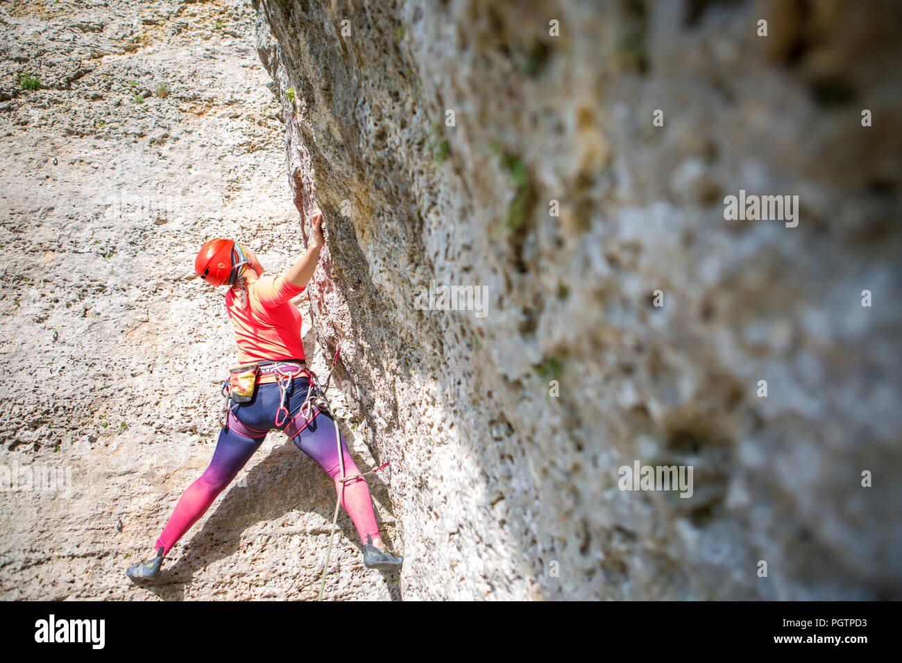 Photo of sports woman in red hard hat with carbine in hand climbing