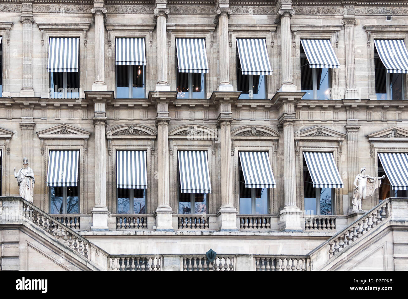 Striped awnings cover windows on an old building with ornate details in Paris France. Stock Photo