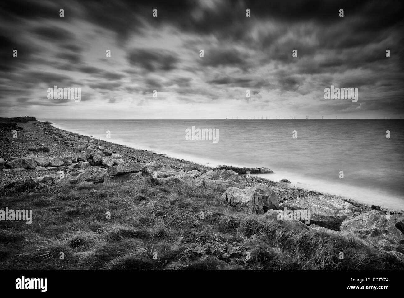 Black and white western shoreline and beach of Walney Island off the Cumbrian coast in summer with long exposure on the sea and shingle beach. Stock Photo