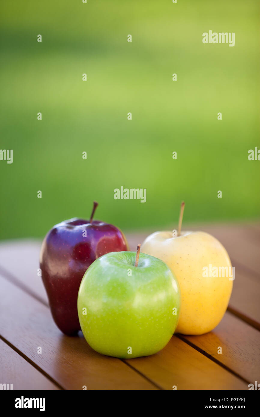 Three different apples on a table with green grass background Stock Photo