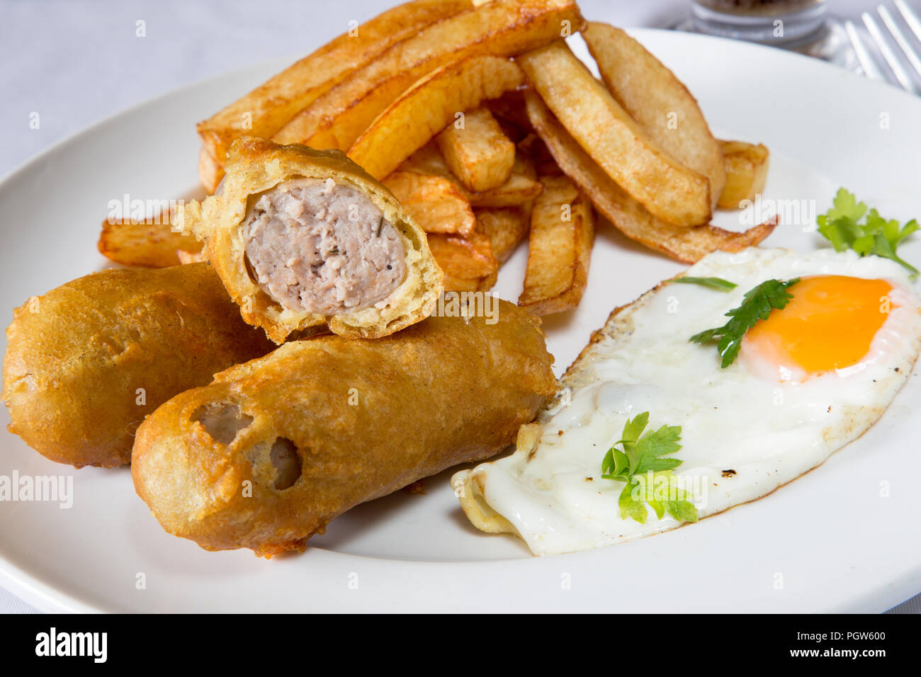 Traditional English supper of deep fried battered sausage with chips/fries and a fried egg Stock Photo