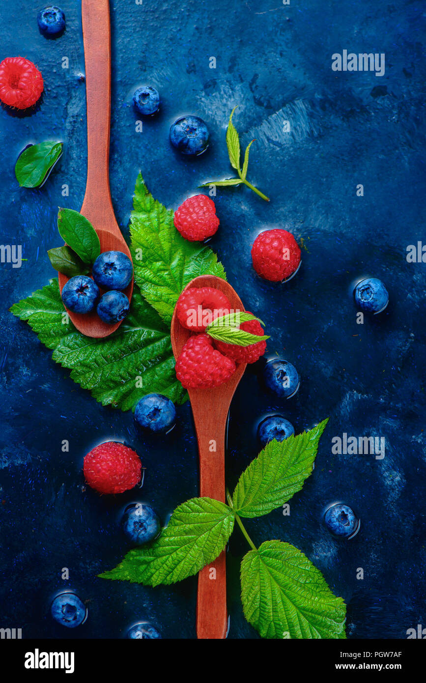 Summer berries in wooden spoons top view. Raspberry and blueberry mix on a dark blue wet background with copy space. Raw ingredients from above Stock Photo