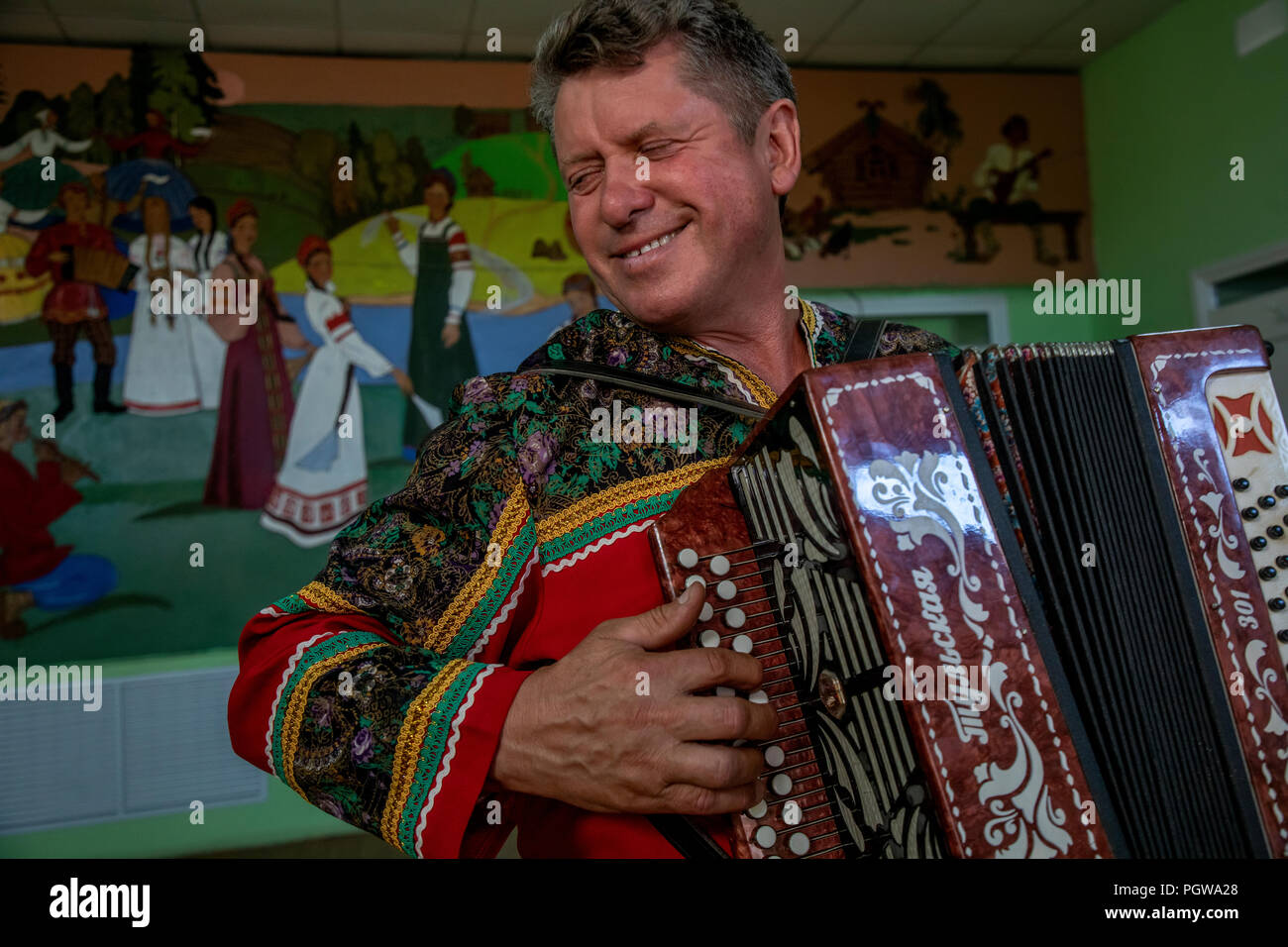 A man in Russian folk costume plays on accordion in a village house of culture of Tambov region, Russia Stock Photo