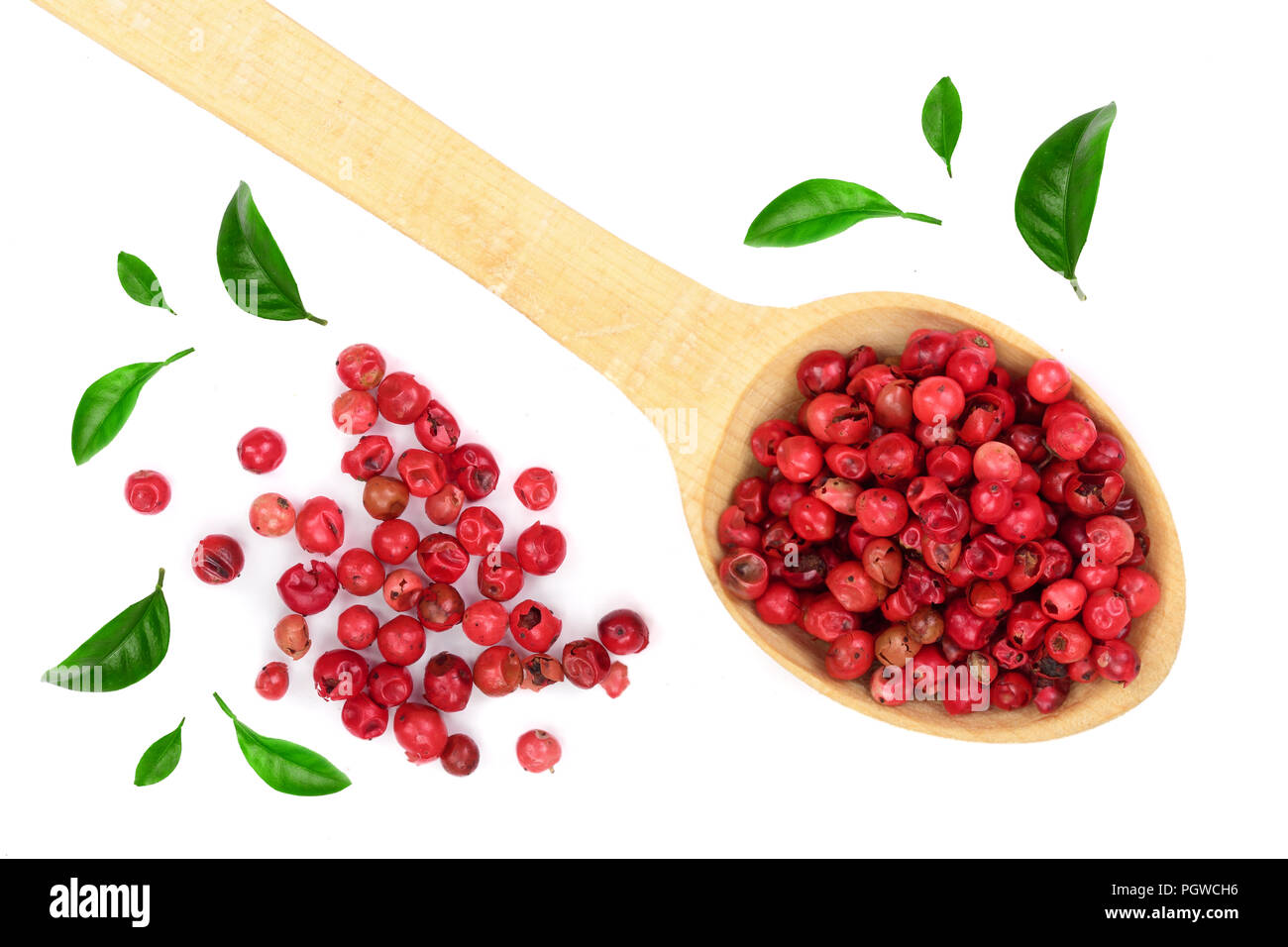 red peppercorns seeds in wooden spoon decorated with green leaves