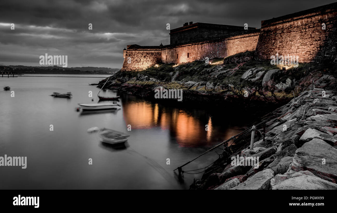Long exposure of the castle of San Anton in A Coruña, night photo, orange lights, stormy sky in port. Stock Photo