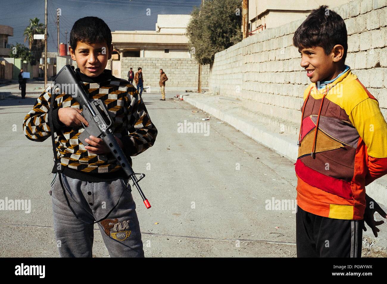 Two children playing the war with a toy M16 on the streets and hug